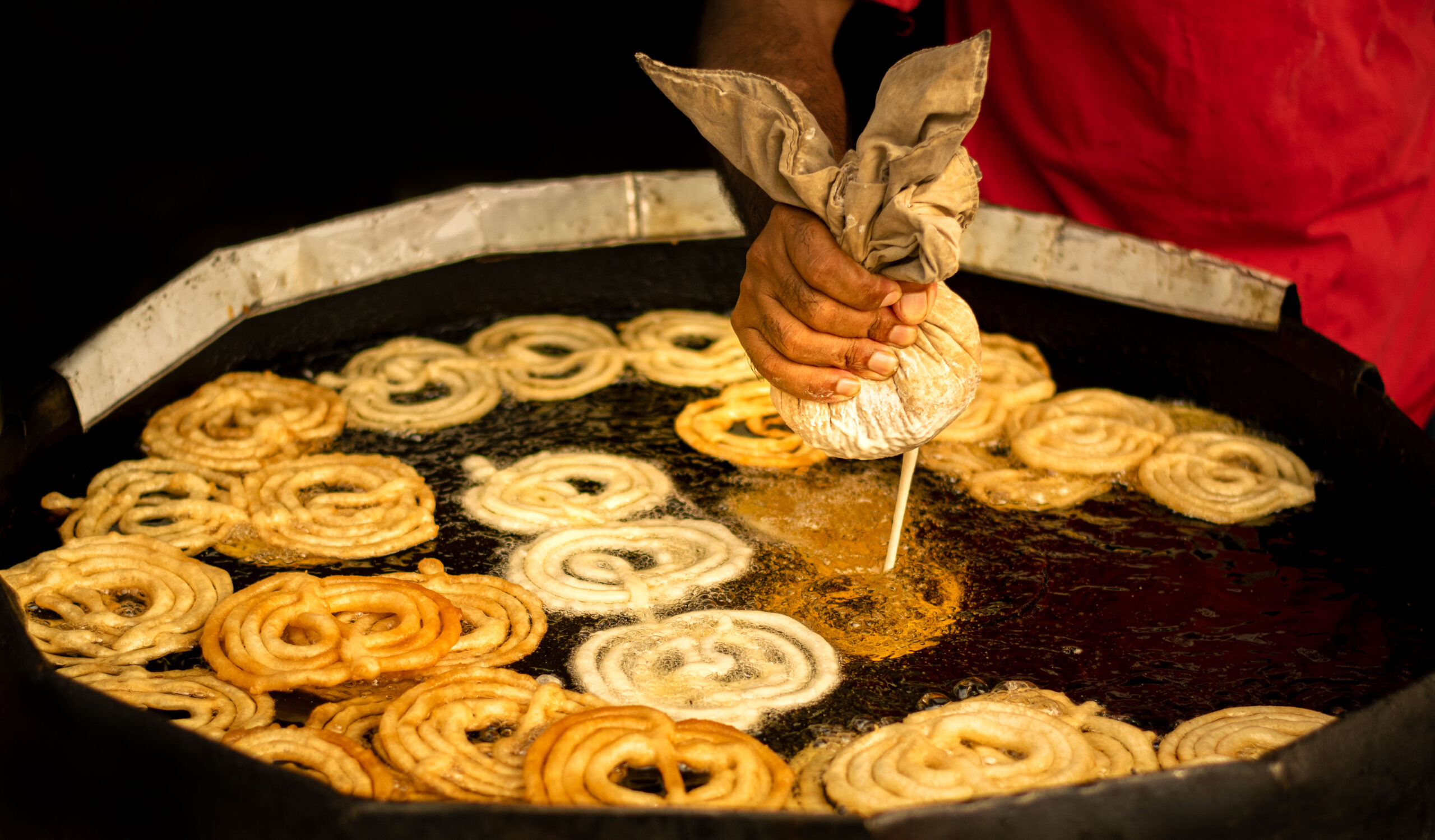 Jalebi batter being piped by hand in a spiral